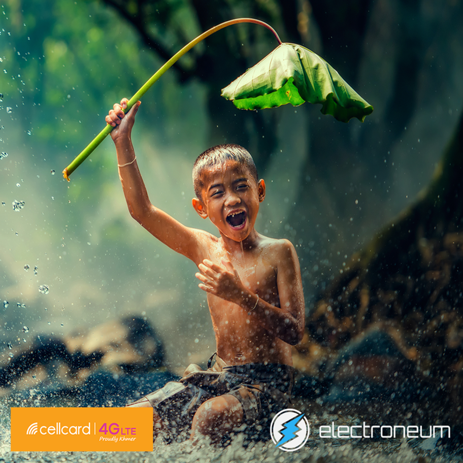 Happy Khmer child under a leaf in a rain storm, promoting Electroneum and Cellcard partnership